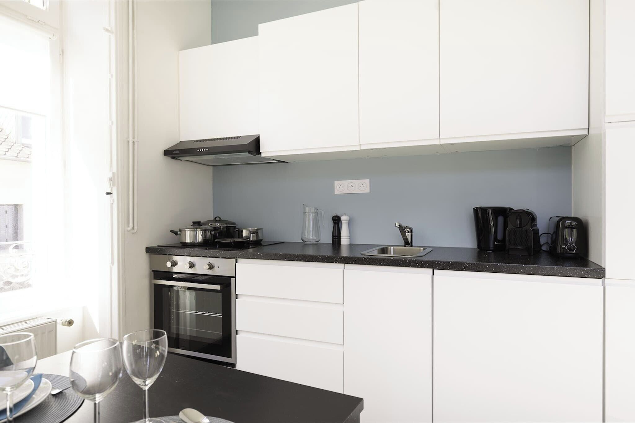 Une cuisine moderne avec des meubles blancs, un plan de travail noir, un four, une cuisinière et une machine à café.