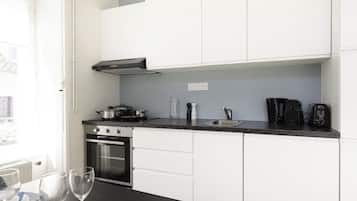 Une cuisine moderne avec des meubles blancs, un plan de travail noir, un four, une cuisinière et une machine à café.