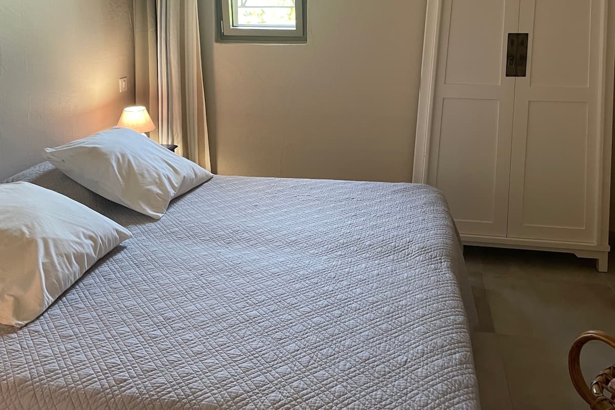 A bedroom with a bed, a window, a wardrobe, and an air conditioning unit.