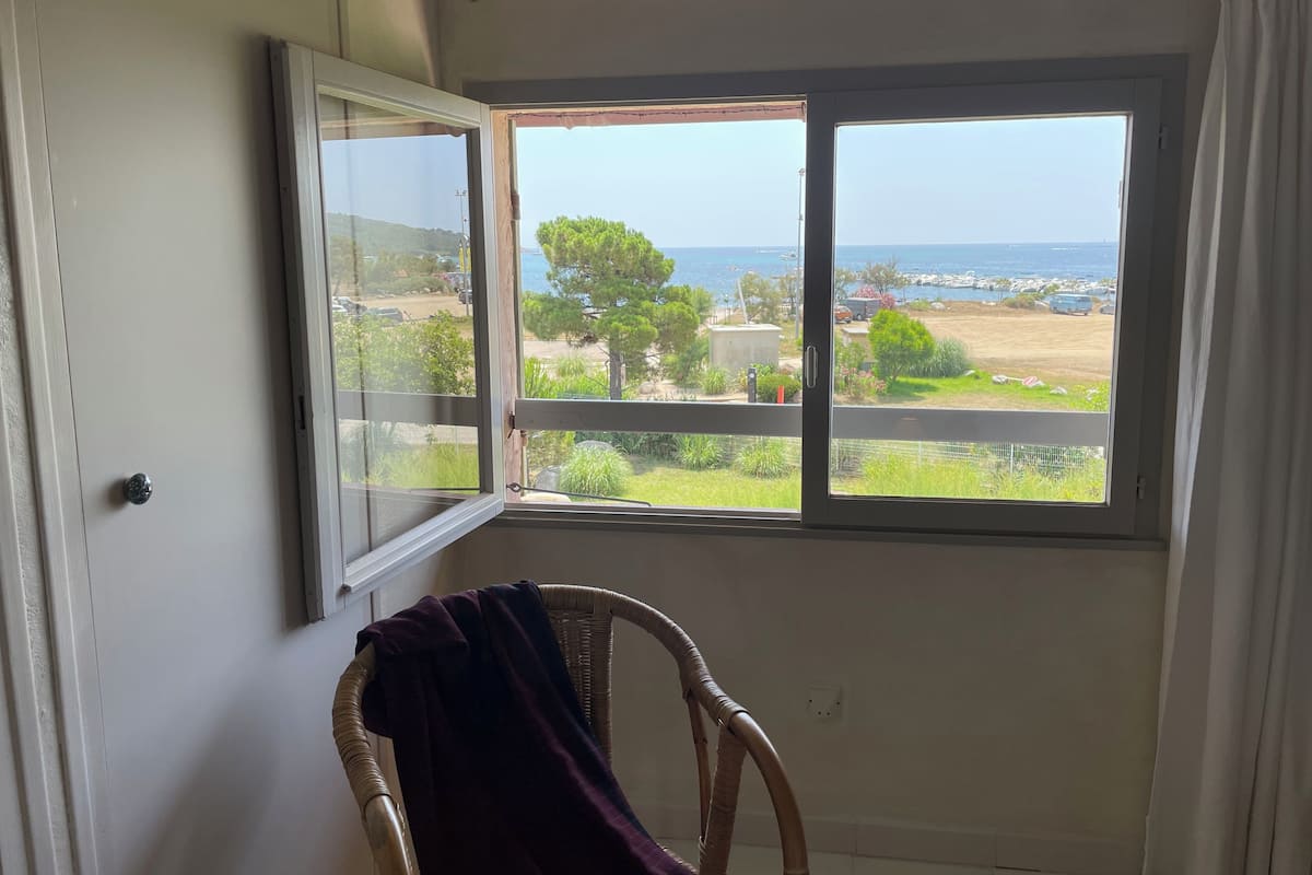 A room with a large window offering a view of the sea and greenery.