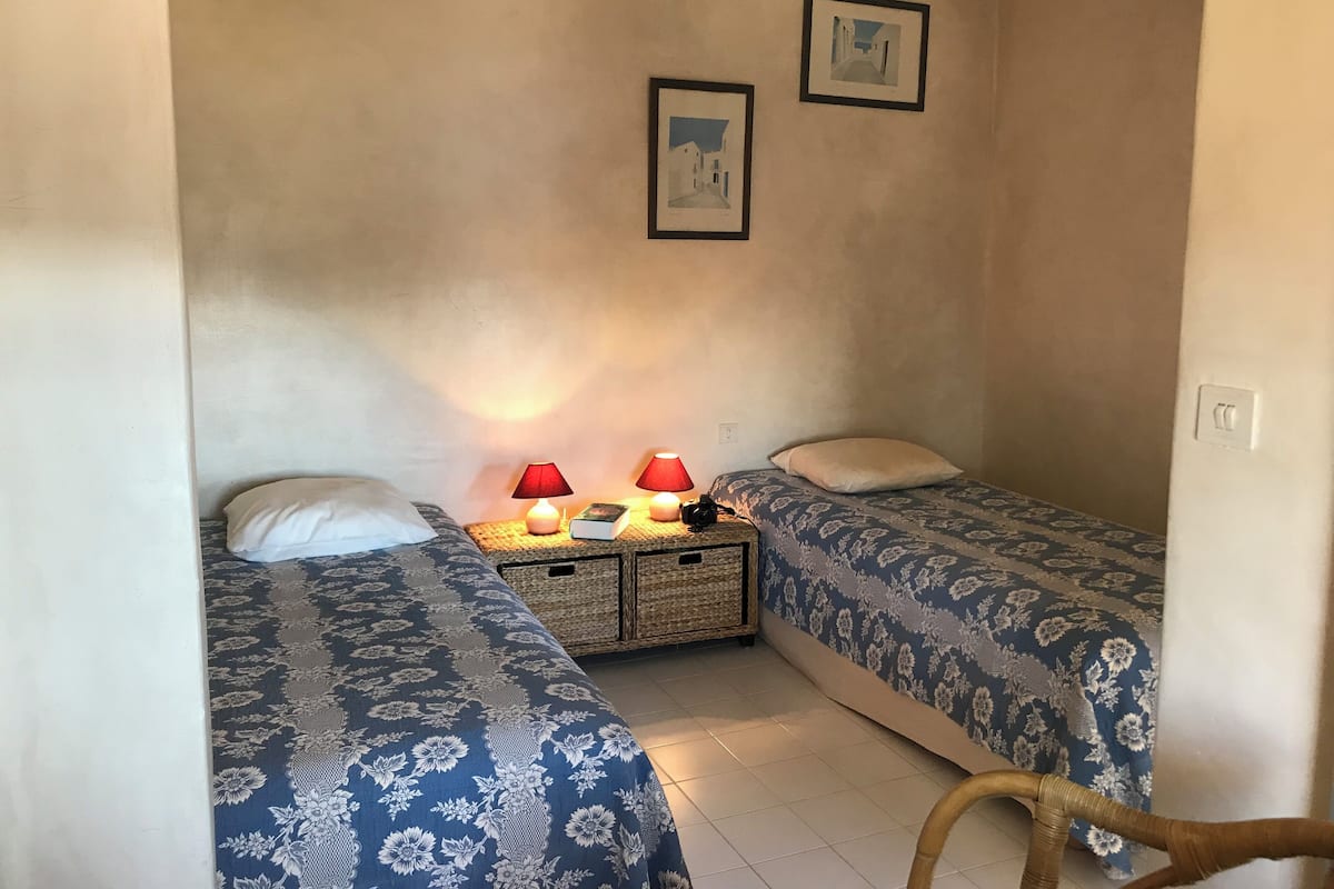A small, cozy room with two beds, a nightstand with lamps, and two framed pictures on the wall.
