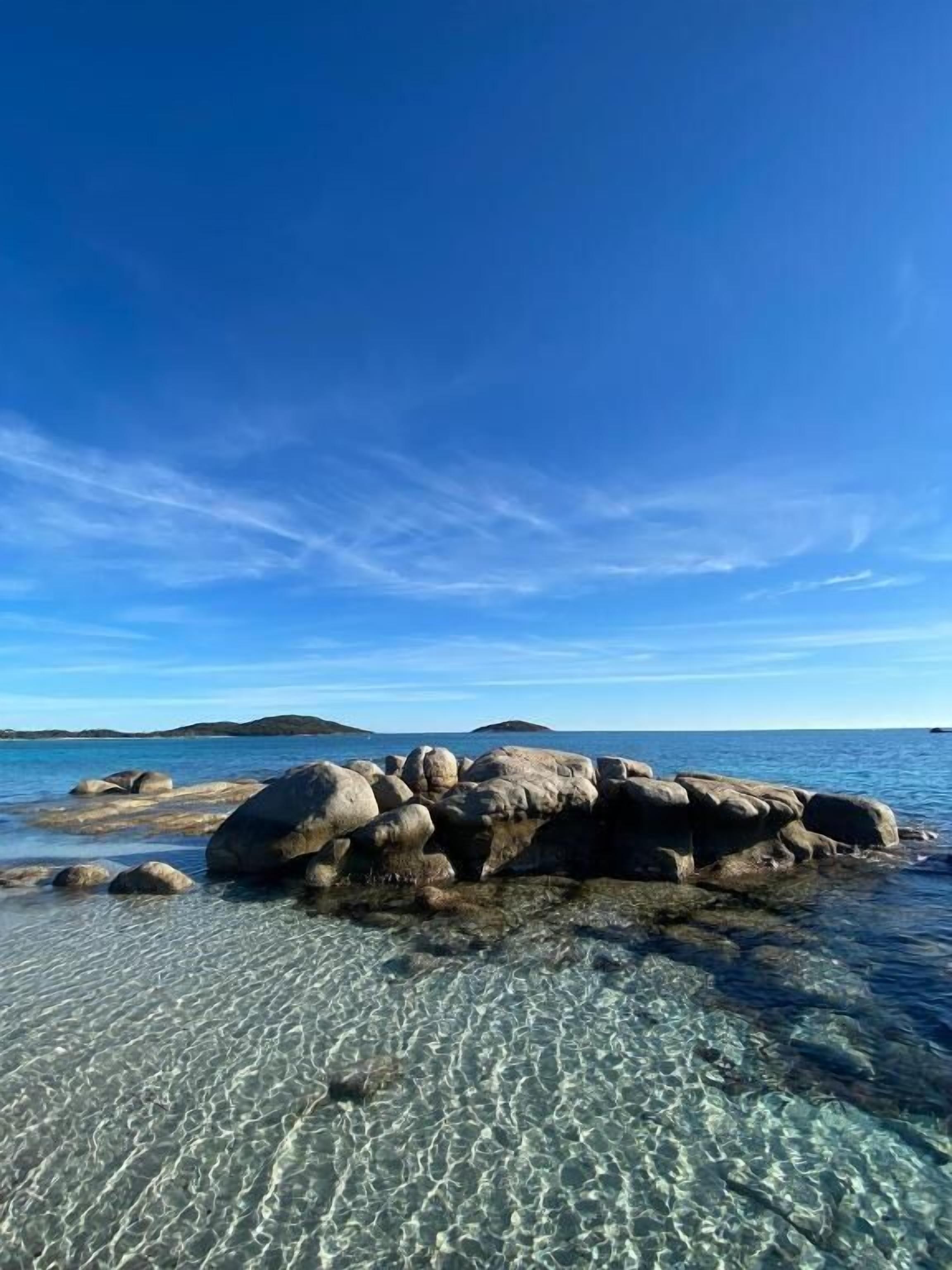 A clear view of a rocky shoreline with calm water and a clear sky.