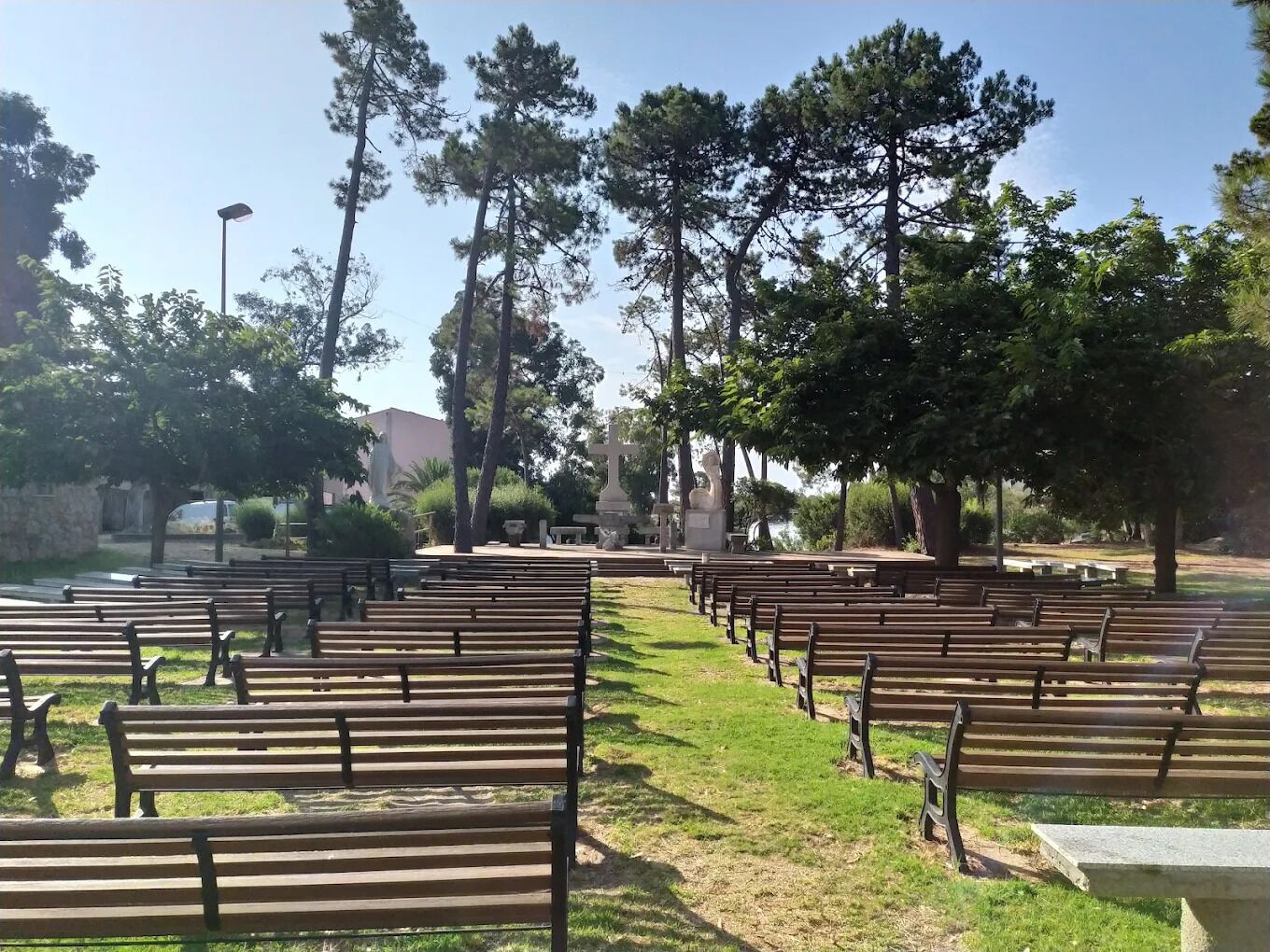 Un espacio al aire libre con hileras de bancos de madera y una estatua central.