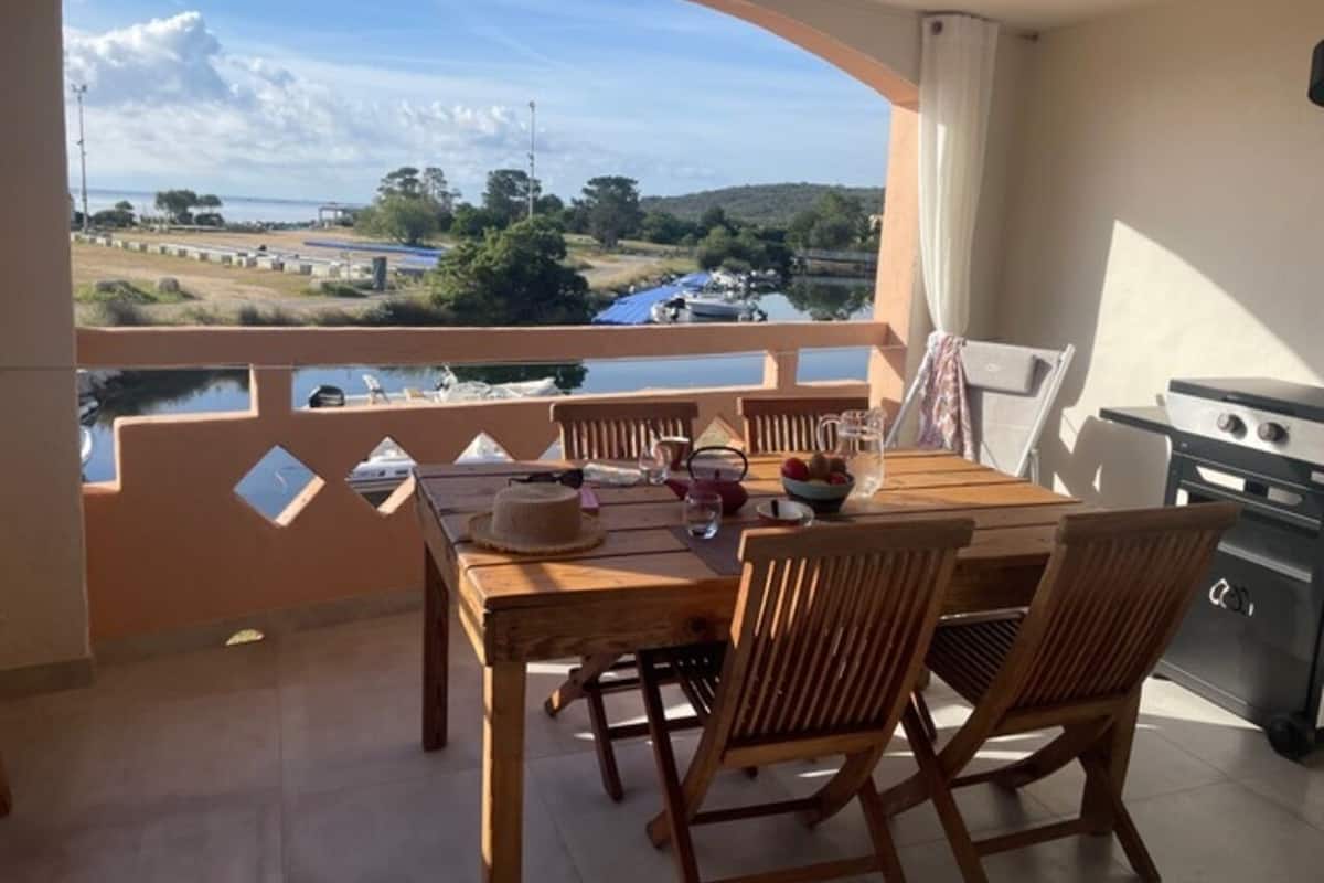 A balcony with a table set for dining, a grill, and a view of a body of water and landscape.