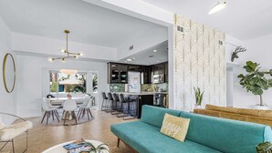 Un salon moderne avec un canapé de couleur turquoise, une table basse et un coin repas comprenant une table et des chaises blanches.