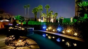 A nighttime pool area with illuminated plants and a hot tub. - Palm Desert Oasis: Pool & Mtn Views (Monthly Rent) (Palm Desert)