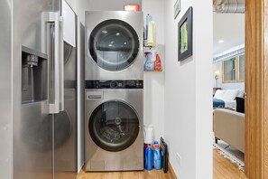 A compact laundry room with a front-loading washer and dryer, a water dispenser, and cleaning supplies on the counter. - NEW! Fully Updated Jr. 1 Bed, Steps from Lincoln Park by AllSet Turnover (Chicago)