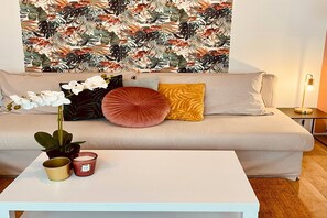 A living room with a sofa, cushions, a coffee table, a plant, and a wall with a tropical leaf pattern. - Scenic Mont-Dore Couple Getaway (Mont-Dore)