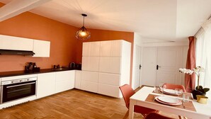 Una cocina compacta con armarios blancos, horno empotrado y comedor con mesa para dos.