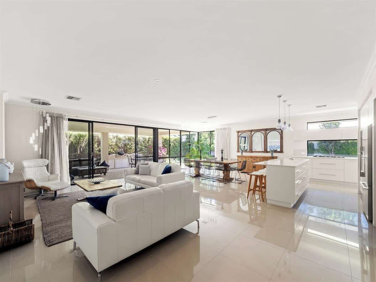 A spacious living area with a white sofa, a dining table, and a kitchen area with white cabinets.