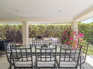 An outdoor patio with a glass table and chairs, surrounded by greenery and a view of trees. - Ile-de-Re: Generous Garden Home by the Beach (Dunsborough)