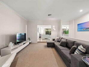 Ein modernes Wohnzimmer mit Flachbildfernseher, grauem Sofa und einer weißen Unterhaltungsanlage.