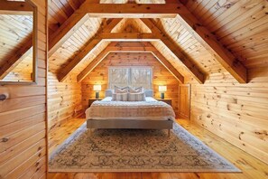 Une chambre avec un plafond en pente, des murs en bois, un lit, deux tables de chevet et un tapis.