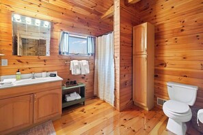 A wooden cabin bathroom with a sink, mirror, vanity, toilet, and shower curtain.