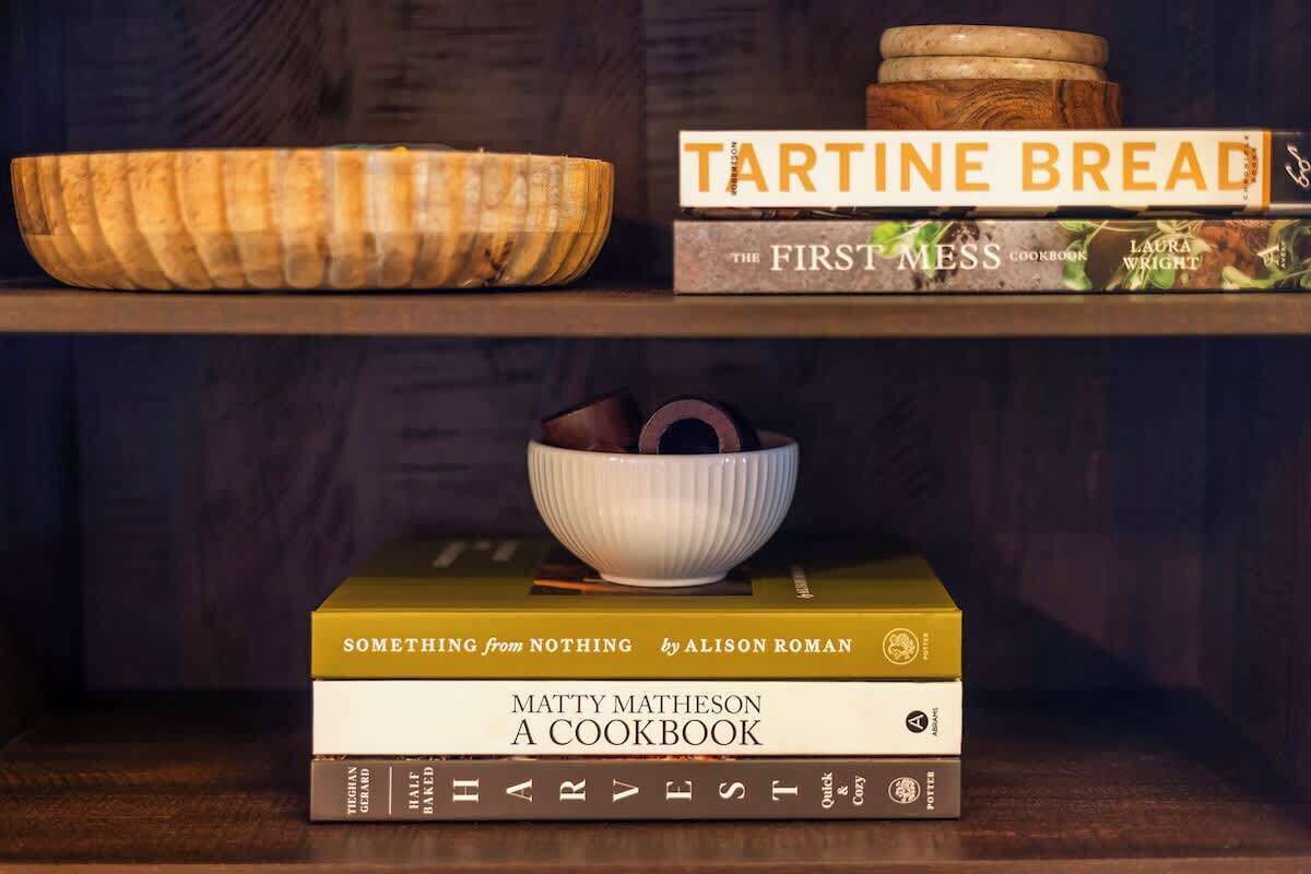 A shelf with a tartine bread book, a tartine bread bowl, and a stack of cookbooks.