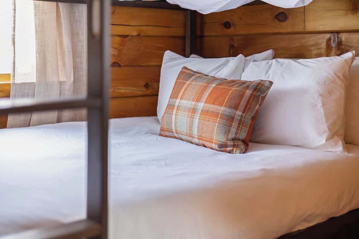 Un letto a castello con biancheria bianca e un cuscino a quadri.