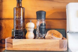 A wooden tray with a bottle of olive oil, a pepper grinder, and a salt shaker.