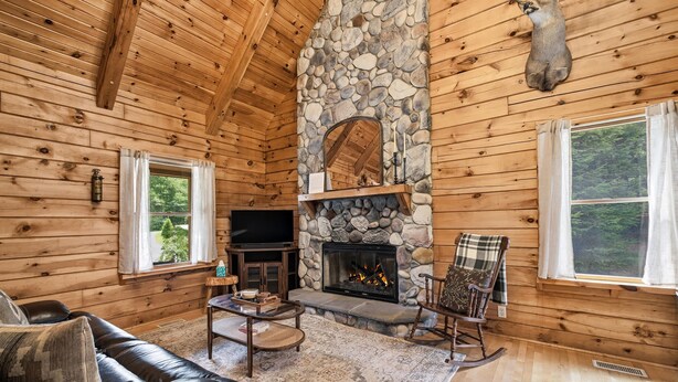 A log cabin interior with a stone fireplace, wooden walls, a leather sofa, and a television. - Private Woodland Retreat w/ Pond, Fireplace & (Watervliet)