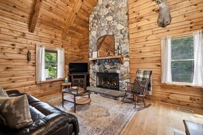 A log cabin interior with a stone fireplace, wooden walls, a leather sofa, and a television. - Private Woodland Retreat w/ Pond, Fireplace & (Watervliet)