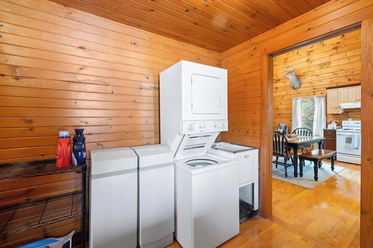 A laundry room with a washer and dryer, wooden walls, a dining area with a table and chairs, and a kitchen visible through an open door.