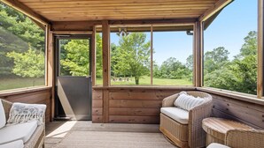 A covered porch with a view of a green landscape, wicker furniture, and a ceiling fan. - Private Woodland Retreat w/ Pond, Fireplace & (Watervliet)