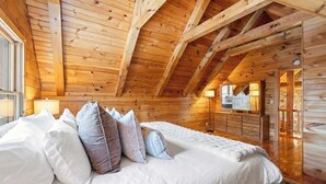 A wooden cabin interior with a bed, pillows, a dresser, and a fireplace. - Private Woodland Retreat w/ Pond, Fireplace & (Watervliet)