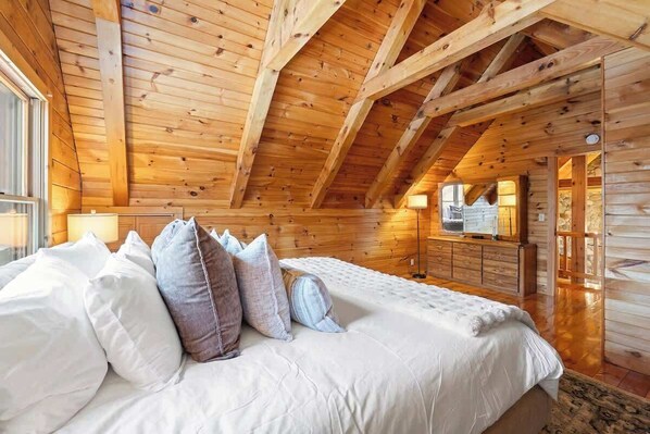 L’intérieur d’un chalet en bois, avec un lit, des oreillers, une commode et une cheminée.