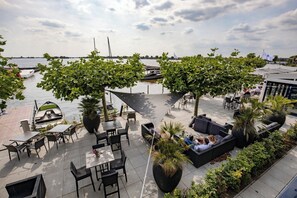 An outdoor seating area with tables and chairs, large planters, and a view of the water with boats. - Relax at a Marina Hotel with Trails, Canoes and a Beautiful Restaurant View (Loosdrecht)