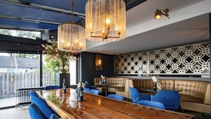 A modern bar area with a wooden bar, blue upholstered seating, and decorative lighting fixtures. - Stay Steps from the Marina with Nature Trails and Locally Inspired Dining (Loosdrecht)