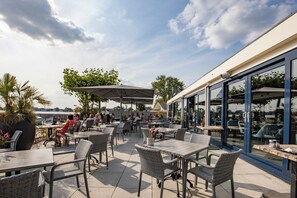 Un patio al aire libre con mobiliario de mimbre, sombrillas y vista a la ciudad.