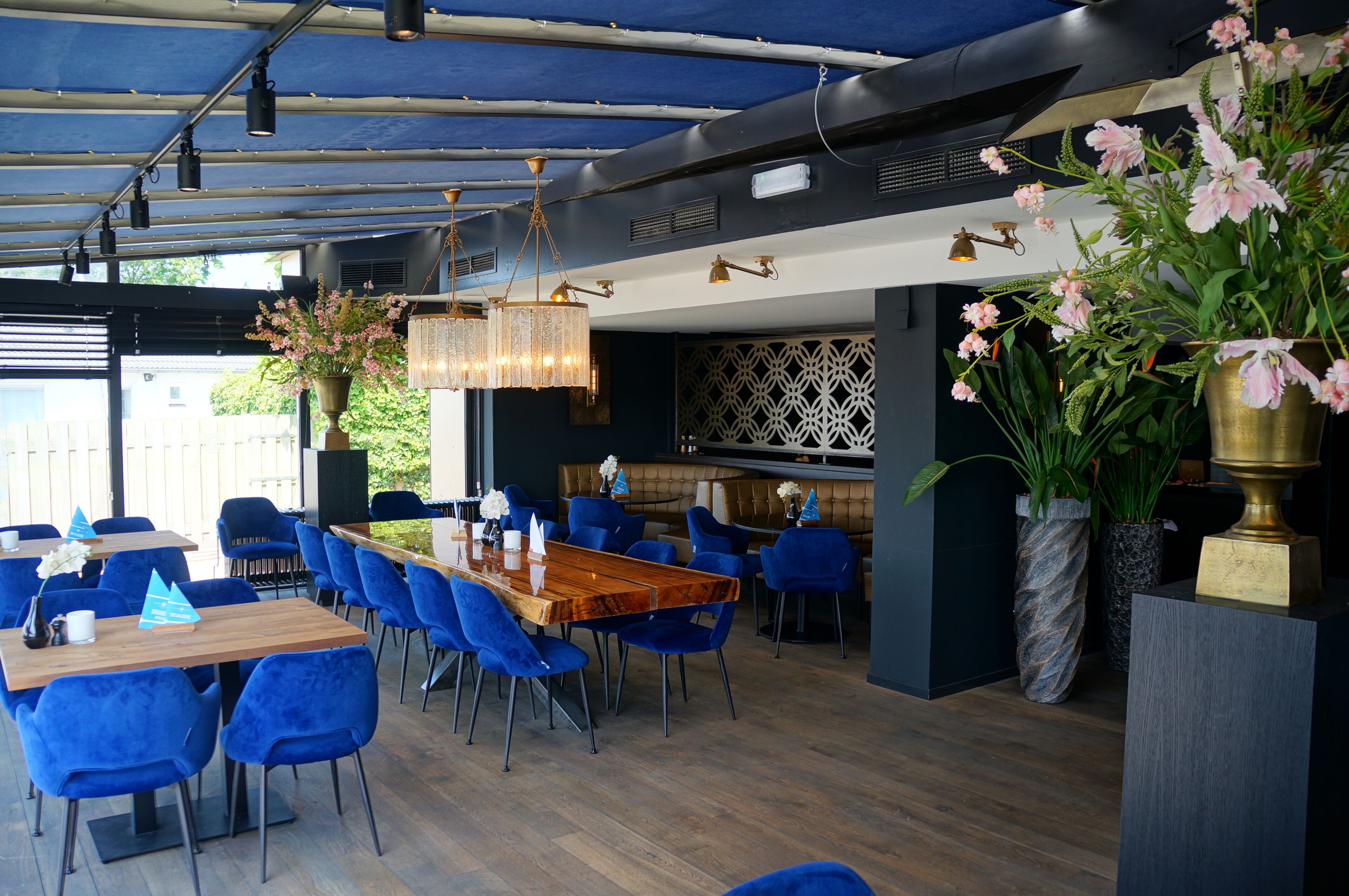 Een modern restaurant met blauwe stoelen, een houten tafel en decoratieve planten.