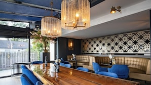 Un espace bar moderne avec un comptoir en bois, des sièges rembourrés en tissu bleu et des luminaires décoratifs.
