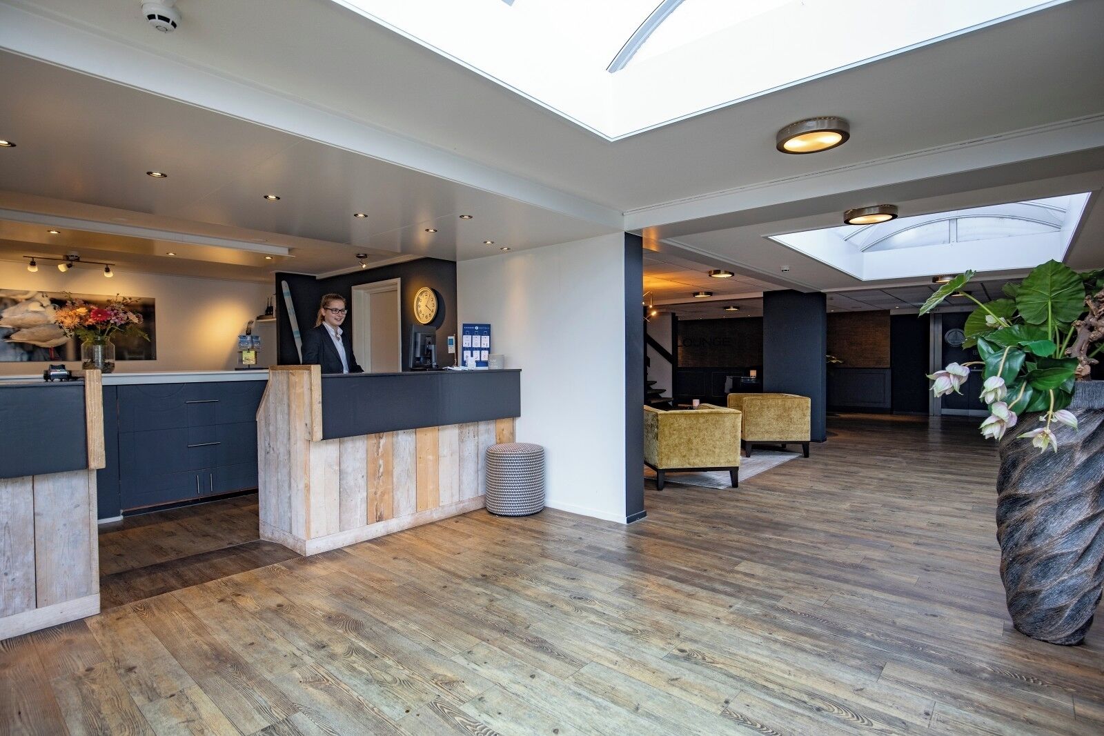 Un hall d’hôtel moderne avec un comptoir d ’accueil, un espace salon et une grande plante.