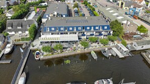 A waterfront hotel with a blue facade, outdoor seating area, and boats docked nearby. - Explore Loosdrecht by Bike, Paddle the Lake and Enjoy Waterfront Dining (Loosdrecht)