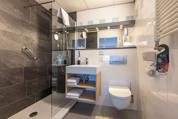 Une salle de bain moderne avec une douche à parois de verre, un lavabo blanc avec un meuble-vasque en bois et des toilettes.