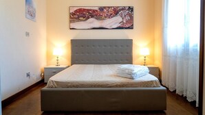 Een slaapkamer met een groot bed, twee nachtkastjes met lampen, een schilderij aan de wand en een raam met gordijnen.