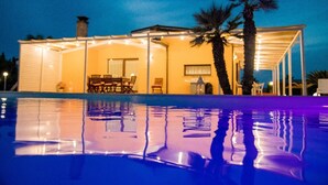 Uitzicht op een zwembad, een huis met overdekt terras, palmbomen en een spiegeling in het water.