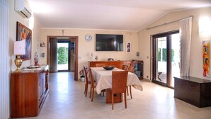 Een eethoek met een tafel voor vier personen, een aan de muur bevestigde televisie en een groot raam met gordijnen.