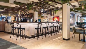 Una zona de bar moderna con una barra larga, varios taburetes y una variedad de utensilios y vasos para bar.