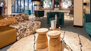 Un área de descanso moderna con un sofá estampado, un sillón verde y taburetes de madera.