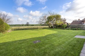 Une pelouse bien entretenue, une clôture en bois, un petit abri de jardin et une maison en arrière-plan.