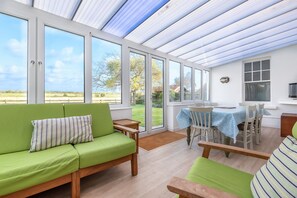 A bright, open-plan living space with a green sofa, wooden furniture, and large windows offering a view of the outdoors. - Nelson Lodge - sleeps 11 guests  in 5 bedrooms (Burnham Market)