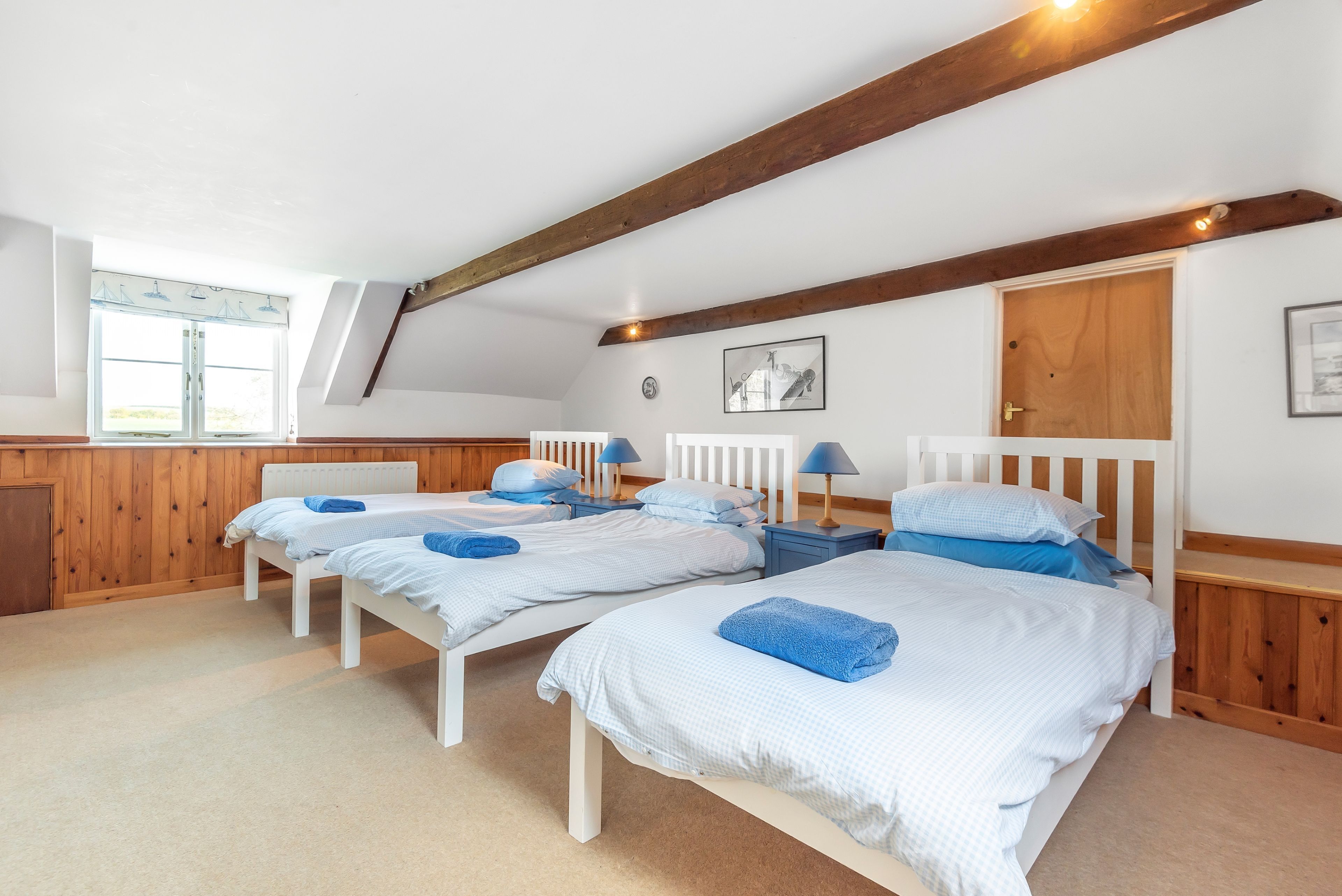 Une chambre avec trois lits simples, des poutres en bois au plafond et une fenêtre avec des stores.
