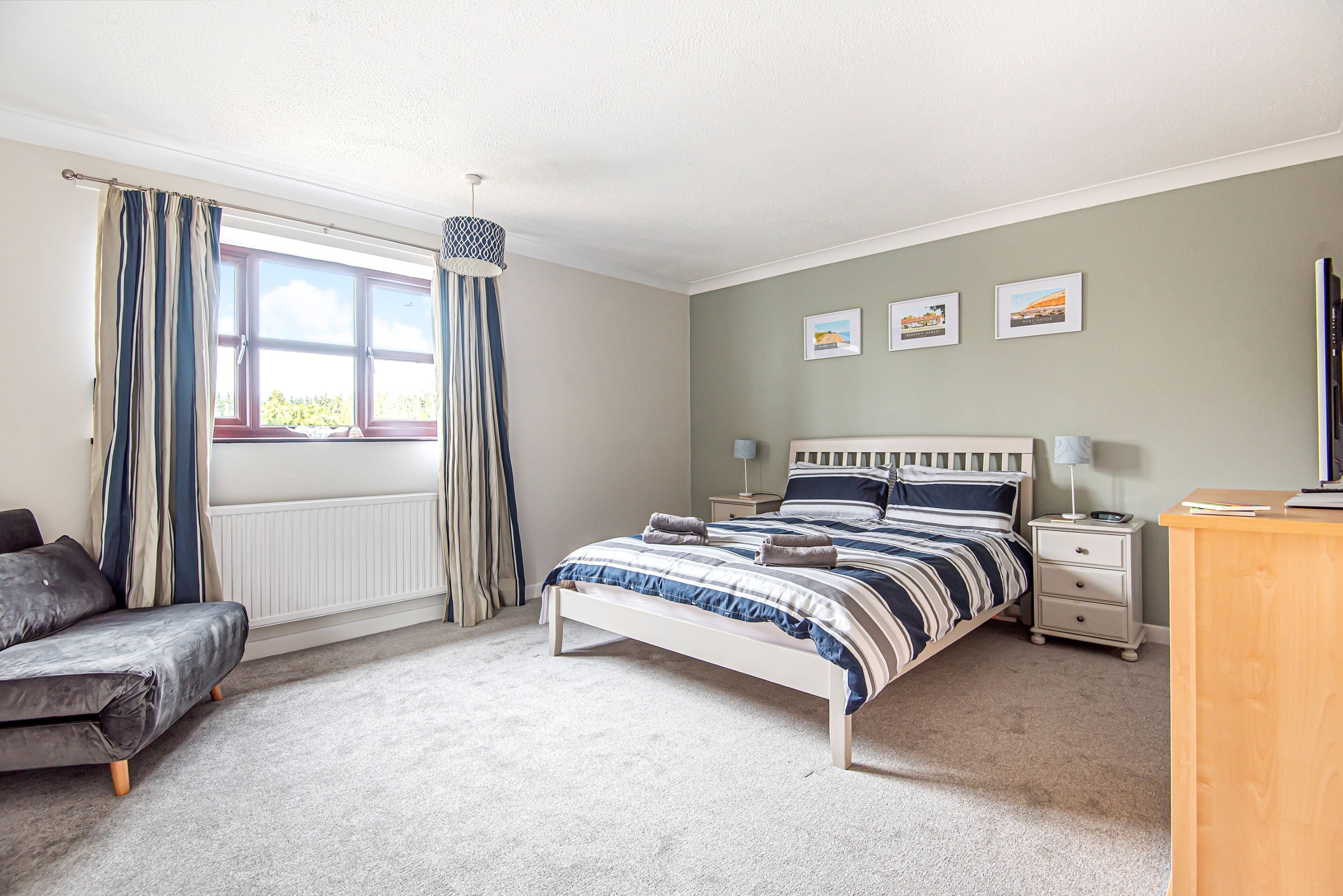 A bedroom with a bed, bedside tables, a nightstand, a chair, and a window with curtains.