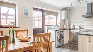 A kitchen with a washing machine, oven, and a dining area with chairs and a table. - Old Hunny Cottage - sleeps 5 guests  in 2 bedrooms (Old Hunstanton)