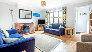 A living room with a fireplace, blue sofa, and a television. - Old Hunny Cottage - sleeps 5 guests  in 2 bedrooms (Old Hunstanton)