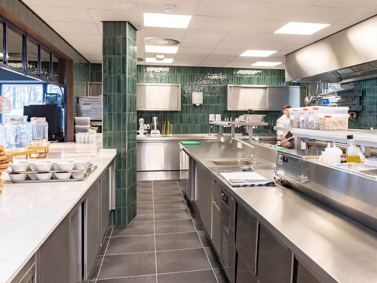 Una cocina moderna con electrodomésticos de acero inoxidable, una isla central y paredes de azulejos verdes.