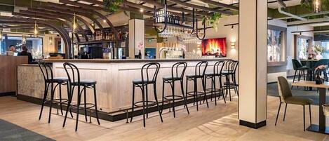 A modern bar area with a long counter, multiple bar stools, and a variety of bar tools and glasses.