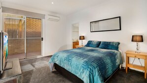 A bedroom with a bed, two bedside tables, a mirror, and a sliding glass door leading to a balcony. - Cowes Beachfront Penthouse (Cowes)