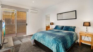 A bedroom with a bed, a nightstand, a lamp, a mirror, and a sliding glass door leading to a balcony. - Cowes Beachfront Penthouse (Cowes)